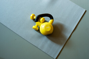 yellow kettlebell and yellow dumbells laying on the grey yoga mat