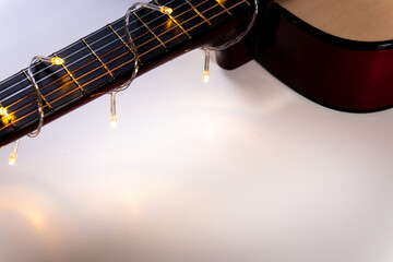 Obraz premium part of a guitar close-up wrapped in a garland on white. Concept on the theme: New Year's sale of musical instruments