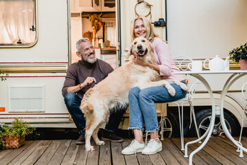 Family photo of mature caucasian couple playing with their retriever in the caravan doorway
