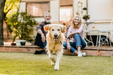 Running dog in the foreground with mature happy couple in the background sitting on the porch with camper van behind