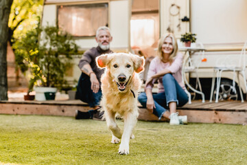 Running dog in the foreground with mature happy couple in the background sitting on the porch with camper van behind - Powered by Adobe