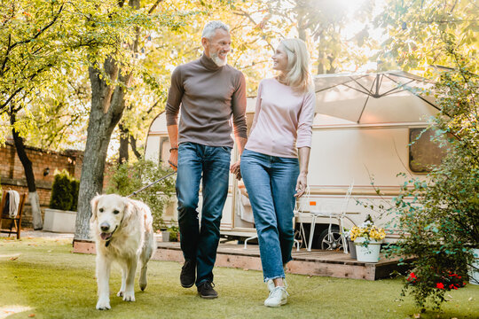 Healthy Mature European Couple Playing With Their Dog In The Park Near Camper Van