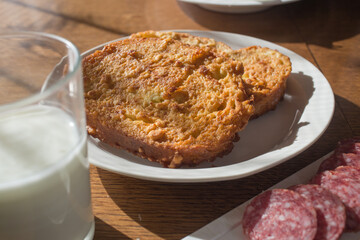 Close up of a french tost with a glass of milk and sausage chopped into pieces on a wooden table.