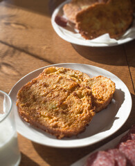 Vertical image of a French toast in close up with milk and slices of  sausage on a wooden table.