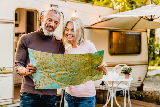 Energetic Elderly European Couple Looking At The Map With Their Caravan Home Behind