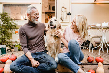 Joyful aged couple petting their dog on the porch of the trailer