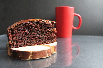 chocolate brownie pie on a wooden stand log cabin back in the background is a red mug a Cup of tea coffee milk on a black background with a copy space for the text Breakfast dessert cafe tea coffee