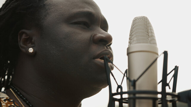 Young african man in traditional colorful clothing singing in the microphone. Close up. High quality photo