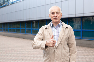 Senior man showing thumbs up outdoors in city landscape near office buildings