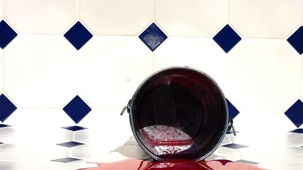 A metal bucket falls to the floor and splashes out the red liquid. - Powered by Adobe