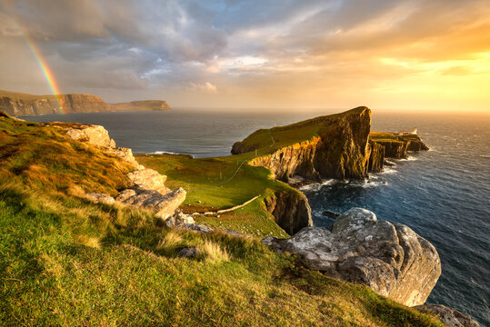Iconic Isle of Skye lighthouse at Neist Point with beautiful golden light and rainbow over coast. 