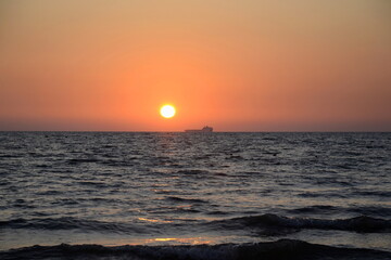 Summertime. Summer beautiful seascape. Sunset on the seashore. Pink sky at sunset. A ship on the horizon
