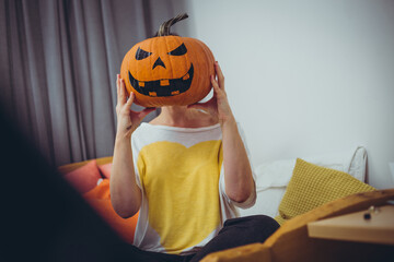 Caucasian female holding big Halloween pumpkin with painted evil face in front of her head