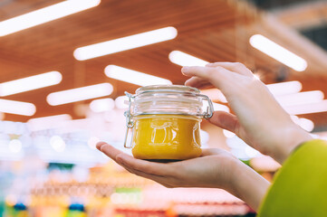 A girl in a supermarket holds a glass jar with honey close-up. against the background of lamps.