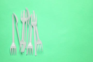 Plastic forks on a green background with a copy of the space. Disposable food appliances
