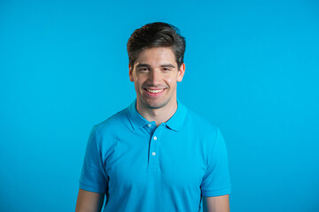 Portrait of smiling cheerful handsome man in blue t-shirt looking to camera. Guy in studio on bright background.