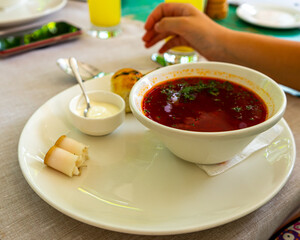 Beet soup in ceramic plate with becon, bread and sour cream on wooden board. Borch, traditional Ukrainian food