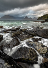 Dramatic Cuillin seascape with dark storm clouds and crashing waves on rocks in foreground. Elgol, Isle of Skye, Scotland, UK.