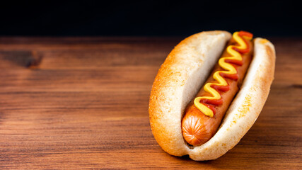 American traditional fast food Hotdog with fresh organic bread bun white wheat and black charcoal sausage ketchup mustard for meal with roasted onion pickle and French fries wedges and coleslaw