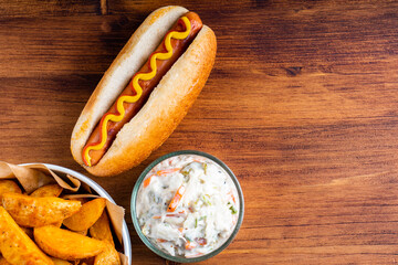 American traditional fast food Hotdog with fresh organic bread bun white wheat and black charcoal sausage ketchup mustard for meal with roasted onion pickle and French fries wedges and coleslaw
