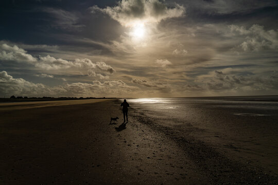 A silhouette of a lady walking a dog on Silloth beach in Cumbria