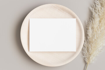 White invitation card mockup on a wooden plate with a pampas grass. 5x7 ratio, similar to A6, A5.