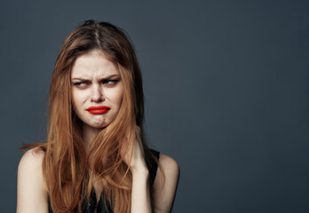 Naklejka premium woman with red lips and in a black sundress on a gray background touches her face with her hands