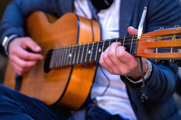 Street music art. Male musician playing the guitar outdoors on the street of old European city. Cigarette burn on the headstock. Selective focus.
