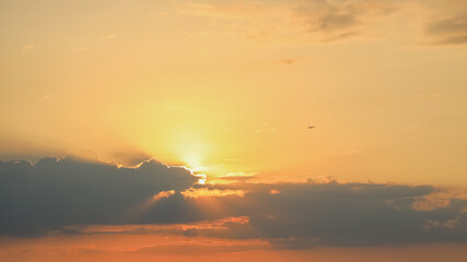 Bright sun rays in the orange sunset sky with cumulus clouds, fantastic atmosphere effects, little bird in the sky as freedom concept