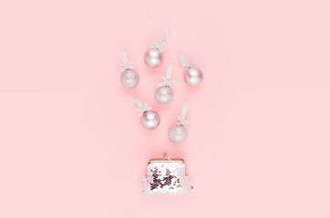 Christmas shopping - silver christmas balls flying above elegant glossy wallet on soft light pastel pink background, copy space.