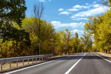 Fototapeta premium Sunny autumn scenic asphalt road way with nice white clouds and colorful trees
