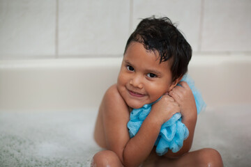 Young child shows that he loves bath time by hugging his wash cloth mesh while soaking his body.