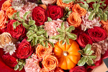 Red and orange flowers with pumpkin. Autumn bouquet of mixed flowers in glass vase on wooden table. The work of the florist at a flower shop. Fresh cut flower.