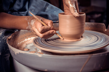 Master-ceramist creates a clay pot on a potter's wheel. Hands of potter close up. Ancient craft and pottery handmade work