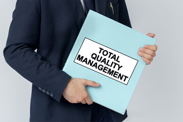 A businessman holds a folder with documents, the text on the folder is - TOTAL QUALITY MANAGEMENT