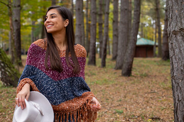 A smiling pretty woman with a hat is walking in the forest and enjoying autumn colors