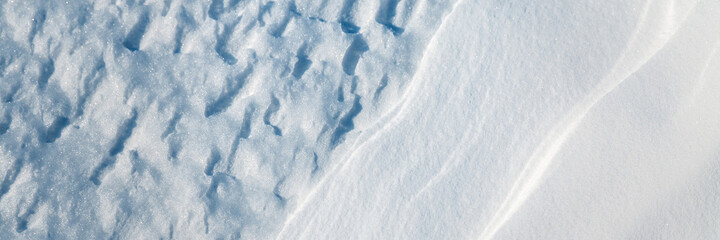 Beautiful winter background with snowy ground. Natural snow texture. Wind sculpted patterns on snow surface. Wide panoramic texture for background and design.