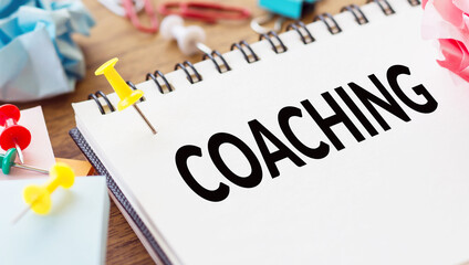 Coaching - text on a notepad with wrinkled paper and paper needles on wooden background