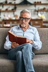 Bearded adult male holding interesting book while resting on the couch at home