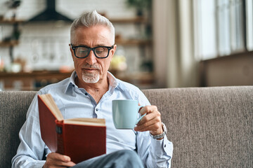 Adult bearded male holding book and enjoying hot drink in his home