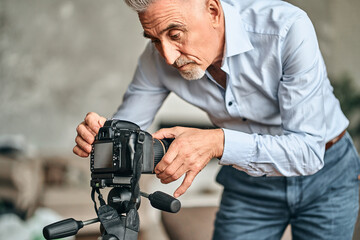 Mature bearded blogger using camera while setting the necessary parameters for shooting