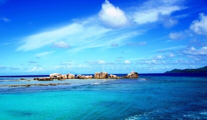 Fototapeta premium Idyllic peaceful azure Indian ocean water surface with granite rocks and spectacular clouds in heaven near exotic paradise Seychelles La Digue island at summertime for happy zen relaxing beach holiday