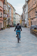 Streets of Bratislava, Slovakia, on a dull day, a female biker is visible riding her bike away from the camera