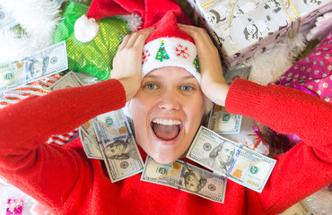 Amazed young woman surrounded by cash money bills and lots of Christmas gifts.