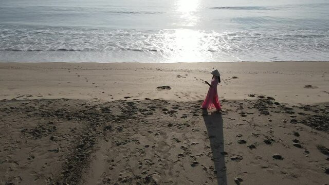 Side and aerial view of woman with Vietnamese costume walk along the beach during sun rise and look happy. Concept of relax and enjoy with holiday outdoor.