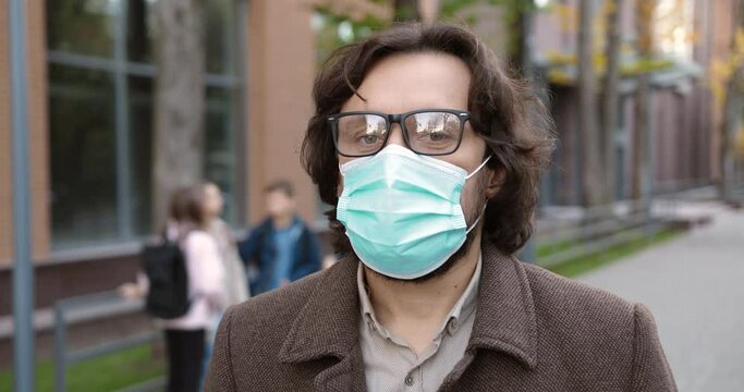 Close Up Portrait Of Happy Caucasian Handsome Man In Mask Standing In Front Of School With Kids On Background. Male Teacher In Glasses Putting Off Mask Outdoors In Quarantine. Back To School Concept