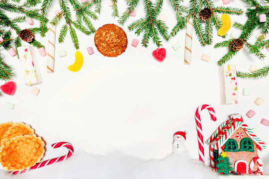 New Year's festive decor on a white background. Fir branches, decoration of red balls, cones, candies, cookie, house and snowman. Free space for text. top view.