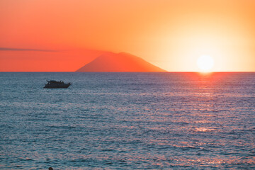 Amazing view of the Stromboli Volcano at sunset, wit the sun going down and amazing sea and sky colors. View form the coast of Calabria, Italy, in the touristic destination of Tropea.