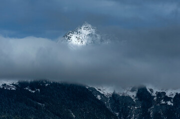 Dramatic Light on a Snow Capped Mountain Peak in the North Cascades. A sliver of light touches just the top of a mountain range surrounded by fog on an early winter morning.
