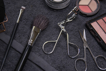 Various cosmetic products on a dark background.Makeup brushes, face shadows in different colors, scissors and chips.

